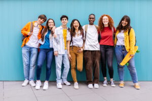 Portrait of seven young student friends leaning on blue wall. Diverse teenage classmates looking at camera standing.