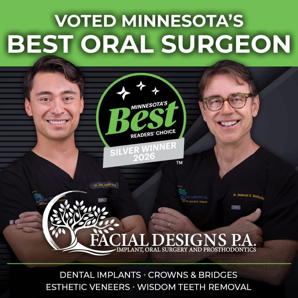 Dr. Clark-Gold (left) and Dr. VanSurksum (right) wearing black medical uniforms stand side by side against a dark blue background with diagonal lines. Both are smiling with arms crossed. Their scrubs display embroidered names and the “Facial Designs P.A.” logo. Above them is a stylized tree‑and‑crescent‑moon logo with the text “Facial Designs P.A. Implant, Oral Surgery and Prosthodontics.