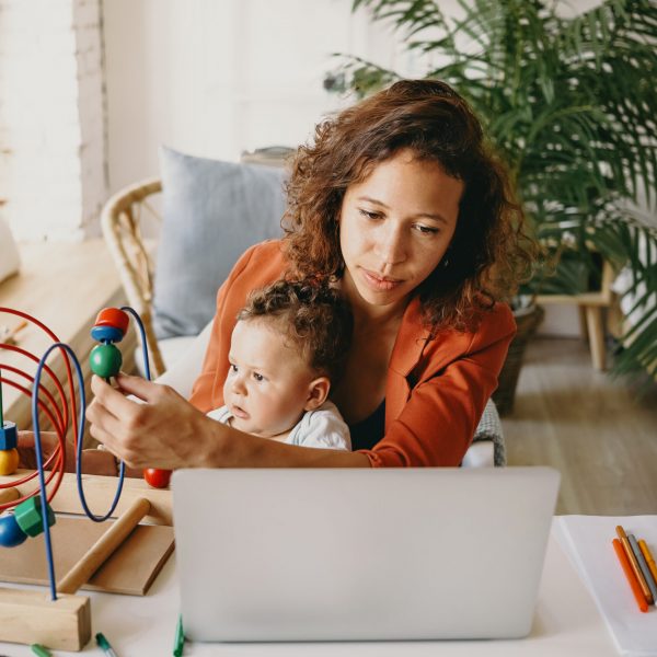 People, maternity, childcare, job and career concept. Portrait of university student girl of mixed race appearance working on research project on laptop pc and playing with her little son at desk