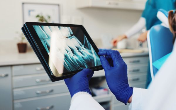 Medical, hands and dentist with xray on tablet screen for help, surgery information or diagnosis. Tech, oral surgeon and person in practice for dental implant, oral scan and tooth alignment procedure